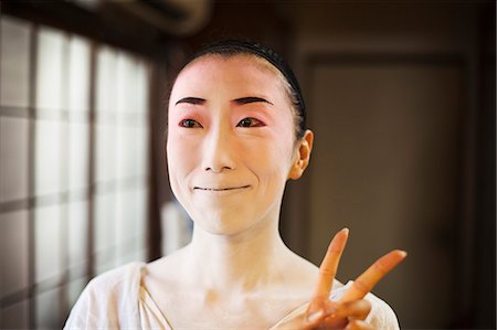 simsearch:6118-08761750,k - Geisha woman with traditional white face makeup and heavy eyeliner holding up two fingers in a modern gesture. Stock Photo - Premium Royalty-Free, Code: 6118-08761782