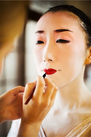 simsearch:6118-08761750,k - A modern woman creating the traditional geisha vivid red lips by painting on lipstick with a fine brush. White face makeup. Stock Photo - Premium Royalty-Free, Code: 6118-08761790