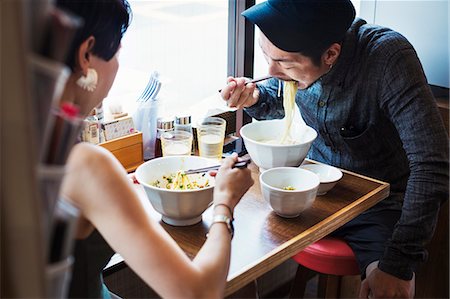 fast food city - A ramen noodle cafe in a city.  A man and woman seated eating noodles from large white bowls. Stock Photo - Premium Royalty-Free, Code: 6118-08761710