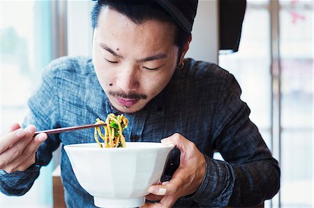 simsearch:6118-08762017,k - A ramen noodle cafe in a city.  A man seated eating ramen noodles from a large broth bowl. Photographie de stock - Premium Libres de Droits, Code: 6118-08761711