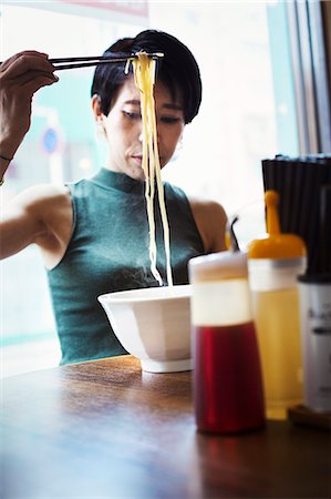 simsearch:6118-09079717,k - A ramen noodle cafe in a city.  A woman seated eating a ramen noodle dish using chopsticks. Stock Photo - Premium Royalty-Free, Code: 6118-08761716