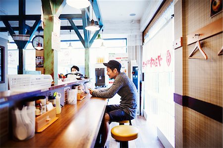 fast food city - A ramen noodle shop in a city. A man seated at a counter looking at his smart phone. Stock Photo - Premium Royalty-Free, Code: 6118-08761718
