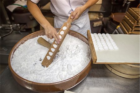 simsearch:859-06537775,k - A small artisan producer of wagashi. A woman chef mixing a large bowl of ingredients and pressing the mixed dough into moulds in a commercial kitchen. Foto de stock - Sin royalties Premium, Código: 6118-08761843