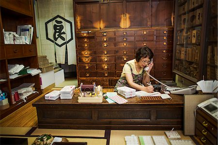 simsearch:6118-08762175,k - A traditional wagashi sweet shop. A woman working at a desk using a laptop and phone. Photographie de stock - Premium Libres de Droits, Code: 6118-08761857