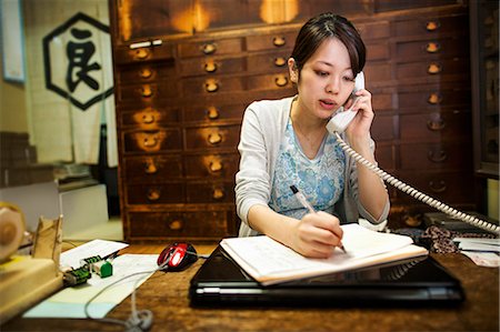 A small artisan producer of specialist treats, sweets called wagashi. A woman taking an order over the telephone and writing with a pen. Stock Photo - Premium Royalty-Free, Code: 6118-08761863