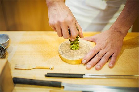 simsearch:6118-08761878,k - A chef working in a small commercial kitchen, an itamae or master chef grating horseradish root for wasabi. Photographie de stock - Premium Libres de Droits, Code: 6118-08761869