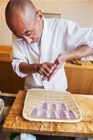 simsearch:6118-08762175,k - A chef working in a small commercial kitchen, an itamae or master chef making sushi, preparing fish. Photographie de stock - Premium Libres de Droits, Code: 6118-08761877