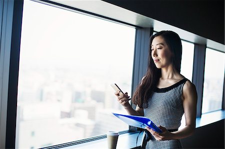 simsearch:6118-08762190,k - A business woman by a window with a view over the city, using her smart phone. Foto de stock - Royalty Free Premium, Número: 6118-08761803