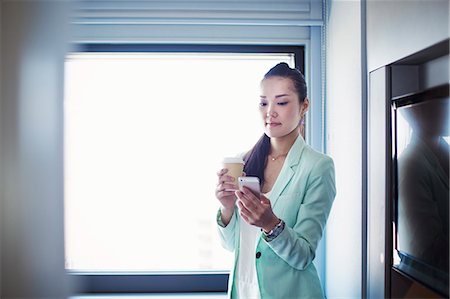 simsearch:6118-08762190,k - A business woman preparing for work, holding a cup of coffee and checking her smart phone. Foto de stock - Royalty Free Premium, Número: 6118-08761801