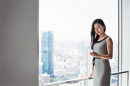 simsearch:6118-08762190,k - A business woman by a window with a view over the city, using her smart phone. Foto de stock - Royalty Free Premium, Número: 6118-08761814