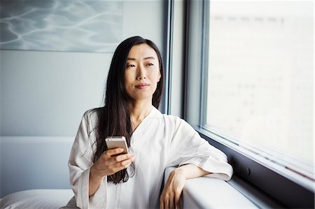 simsearch:6118-08762190,k - A business woman preparing for work, sitting by a window in her nightclothes, holding a smart phone. Foto de stock - Royalty Free Premium, Número: 6118-08761827