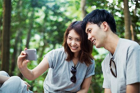 simsearch:6118-08762190,k - Young woman and a man sitting in a forest, taking a selfie. Foto de stock - Royalty Free Premium, Número: 6118-08761952