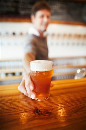 Beer glass standing on a counter, man in the background. Stock Photo - Premium Royalty-Free, Code: 6118-08761912