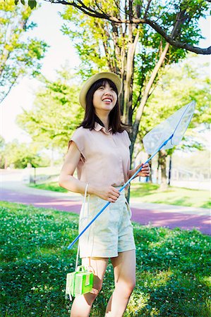 Young woman with long brown hair standing in a park, holding a butterfly net. Fotografie stock - Premium Royalty-Free, Codice: 6118-08762052