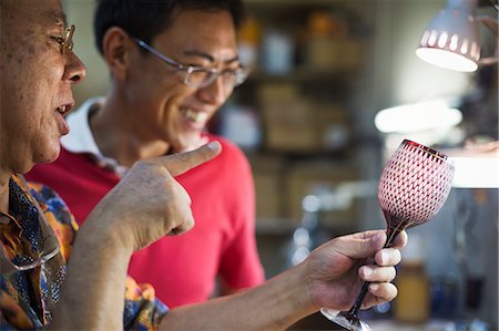 simsearch:6118-08659947,k - Two people, a father and son at work in a glass maker's studio workshop, inspecting a red cut glass wine glass. Stockbilder - Premium RF Lizenzfrei, Bildnummer: 6118-08762084