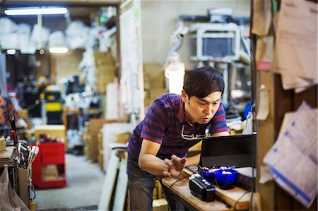 simsearch:6118-09079486,k - A man using a laptop computer, working in a glass maker's workshop. Foto de stock - Royalty Free Premium, Número: 6118-08762091