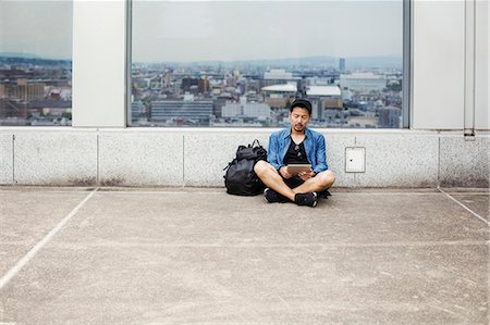 simsearch:6118-08762190,k - A man sitting on the floor using his smart phone, in front of a viewing point window on to a city. Foto de stock - Royalty Free Premium, Número: 6118-08762185