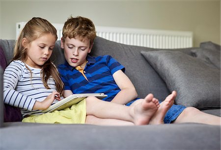 simsearch:6118-07913336,k - Two children seated sharing a digital tablet watching the screen. Stock Photo - Premium Royalty-Free, Code: 6118-08797595
