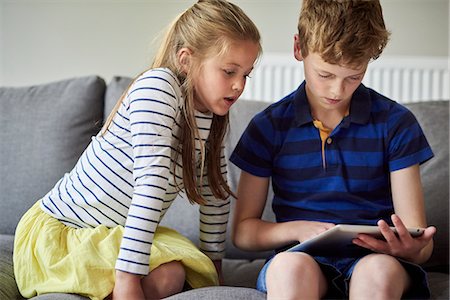 simsearch:6118-07913336,k - Two children seated sharing a digital tablet watching the screen. Stock Photo - Premium Royalty-Free, Code: 6118-08797596
