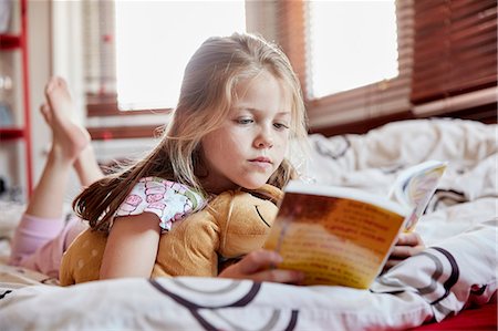 single bed - A girl lying on her bed on her front, reading a book. Stock Photo - Premium Royalty-Free, Code: 6118-08797609