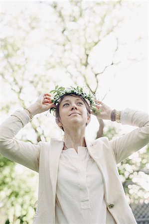 simsearch:6118-08725521,k - Woman standing in a garden, putting a flower wreath in her hair. Stock Photo - Premium Royalty-Free, Code: 6118-08725527