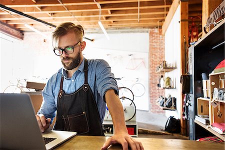 small business owner on computer not looking at camera - A man in a bicycle repair shop using a laptop computer.  Running a business. Stock Photo - Premium Royalty-Free, Code: 6118-08725679