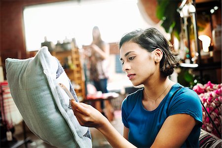 simsearch:6118-07440349,k - Woman standing in a shop holding a cushion, reading the price tag. Stock Photo - Premium Royalty-Free, Code: 6118-08725759