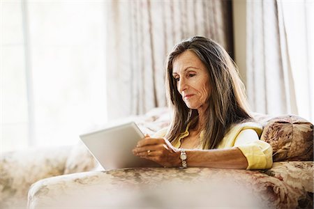 simsearch:6118-07966891,k - Senior woman with long brown hair sitting on a sofa, using a digital tablet. Photographie de stock - Premium Libres de Droits, Code: 6118-08725764