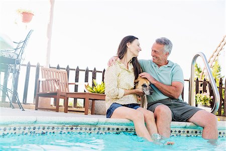 simsearch:6118-08725493,k - A couple sitting on the edge of a swimming pool, with their dog between them. Stock Photo - Premium Royalty-Free, Code: 6118-08725781