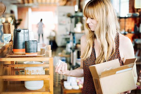 Woman in a shop, holding a small cardboard box with merchandise. Photographie de stock - Premium Libres de Droits, Code: 6118-08725714