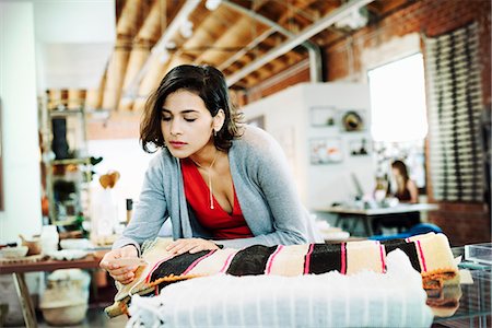 Young woman in a shop, looking at the price tag of a small striped rug. Stock Photo - Premium Royalty-Free, Code: 6118-08725726