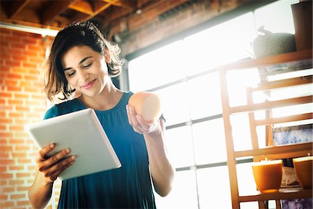 Young woman in a shop, holding a digital tablet and a scented candle. Stock Photo - Premium Royalty-Free, Code: 6118-08725738