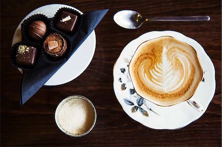 Assorted hand made chocolates on a plate.  A cup of coffee with a pattern in the foam top. Stock Photo - Premium Royalty-Free, Code: 6118-08725937