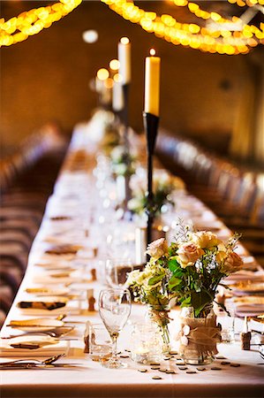 A wedding venue decorated for a party, with fairy lights and a long table set for dinner. Stock Photo - Premium Royalty-Free, Code: 6118-08726047