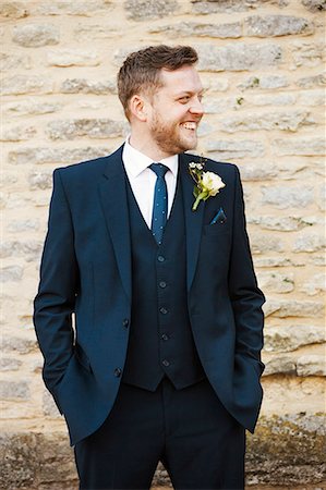 A man in a suit with a buttonhole with his hands in his pockets, smiling. Stock Photo - Premium Royalty-Free, Code: 6118-08726051