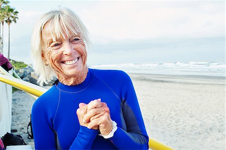 Smiling senior woman wearing a wetsuit, standing on a sandy beach. Photographie de stock - Premium Libres de Droits, Code: 6118-08726065