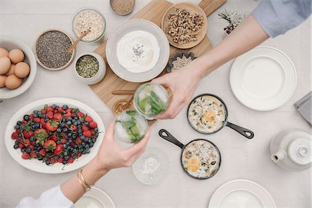 simsearch:6118-07440680,k - Breakfast. Overhead view of dishes of fruit, berries and yoghurt, eggs and cooked omelettes. Two people reaching to dish out food. Foto de stock - Royalty Free Premium, Número: 6118-08726026