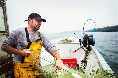 A fisherman on a boat hauling in the fishing net. Photographie de stock - Premium Libres de Droits, Code: 6118-08726032