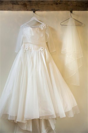 A long white wedding dress with full skirt, petticoats and veil on a hanger, hanging from a hook. Stock Photo - Premium Royalty-Free, Code: 6118-08726035