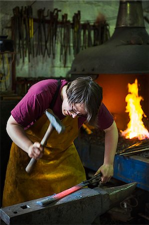 simsearch:6118-08729041,k - A blacksmith strikes a length of red hot metal on an anvil with a hammer in a workshop. Stock Photo - Premium Royalty-Free, Code: 6118-08729043