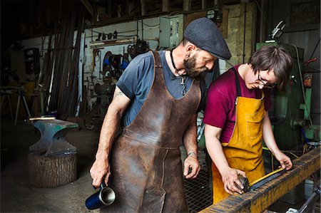 Two blacksmiths measure a length of metal in a workshop. Photographie de stock - Premium Libres de Droits, Code: 6118-08729045