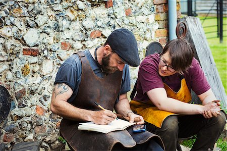 schmied - Two men wearing aprons writing into a notebook sat in a garden. Stockbilder - Premium RF Lizenzfrei, Bildnummer: 6118-08729048