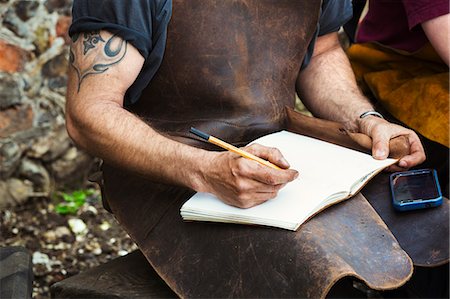 drawing (artwork) - Two people, man and woman blacksmiths wearing leather aprons writing into a notebook sat in a garden. Stock Photo - Premium Royalty-Free, Code: 6118-08729049