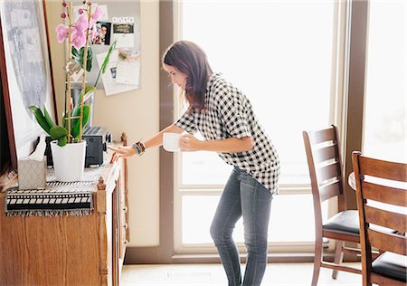 simsearch:6118-08729154,k - Woman with long brown hair, wearing a chequered shirt and jeans, holding a mug, switching on stereo. Foto de stock - Sin royalties Premium, Código: 6118-08729153