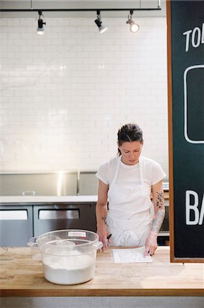 Woman wearing a white apron standing at a work counter in a bakery. Stock Photo - Premium Royalty-Free, Code: 6118-08729178