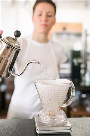 Woman wearing a white apron standing in a coffee shop, making filter coffee. Stock Photo - Premium Royalty-Free, Code: 6118-08729130