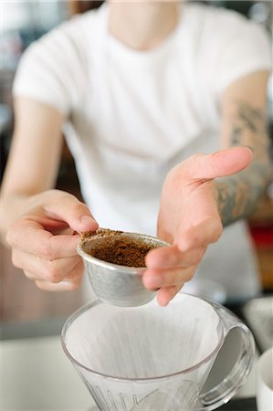 Woman wearing a white apron standing in a coffee shop, making filter coffee. Stock Photo - Premium Royalty-Free, Code: 6118-08729131