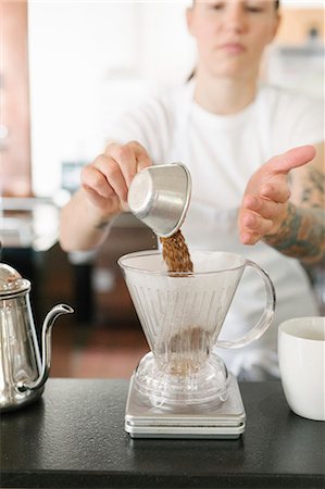 Woman wearing a white apron standing in a coffee shop, making filter coffee. Stock Photo - Premium Royalty-Free, Code: 6118-08729132