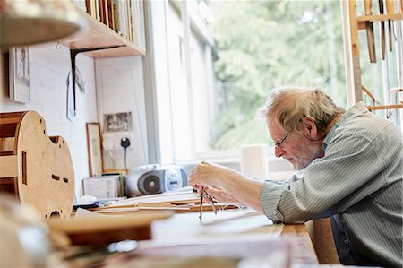 A violin maker at his drawing board drawing out the plans and outline for a new instrument. Photographie de stock - Premium Libres de Droits, Code: 6118-08729262