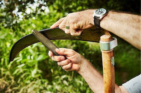 simsearch:6118-08729266,k - A gardener working sharpening a curved metal scythe blade with a file. Stockbilder - Premium RF Lizenzfrei, Bildnummer: 6118-08729272